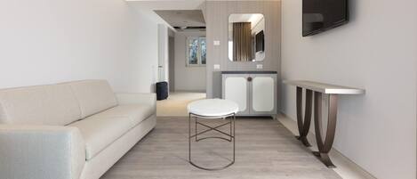 Una habitación de hotel moderna con sofá, una mesa redonda, un televisor montado en la pared y un espejo sobre la mesa.