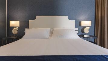 Una cama bien tendida con sábanas blancas, dos mesitas de noche con lámparas y una pared azul oscuro.