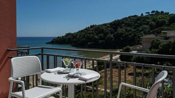 A balcony with a white table and chairs, overlooking a coastal landscape with trees and a clear sky.