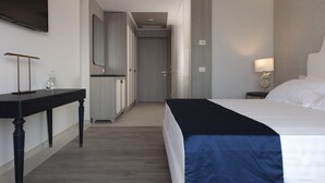 Una habitación de hotel con cama, mesita de noche, lámpara y televisor montado en la pared.
