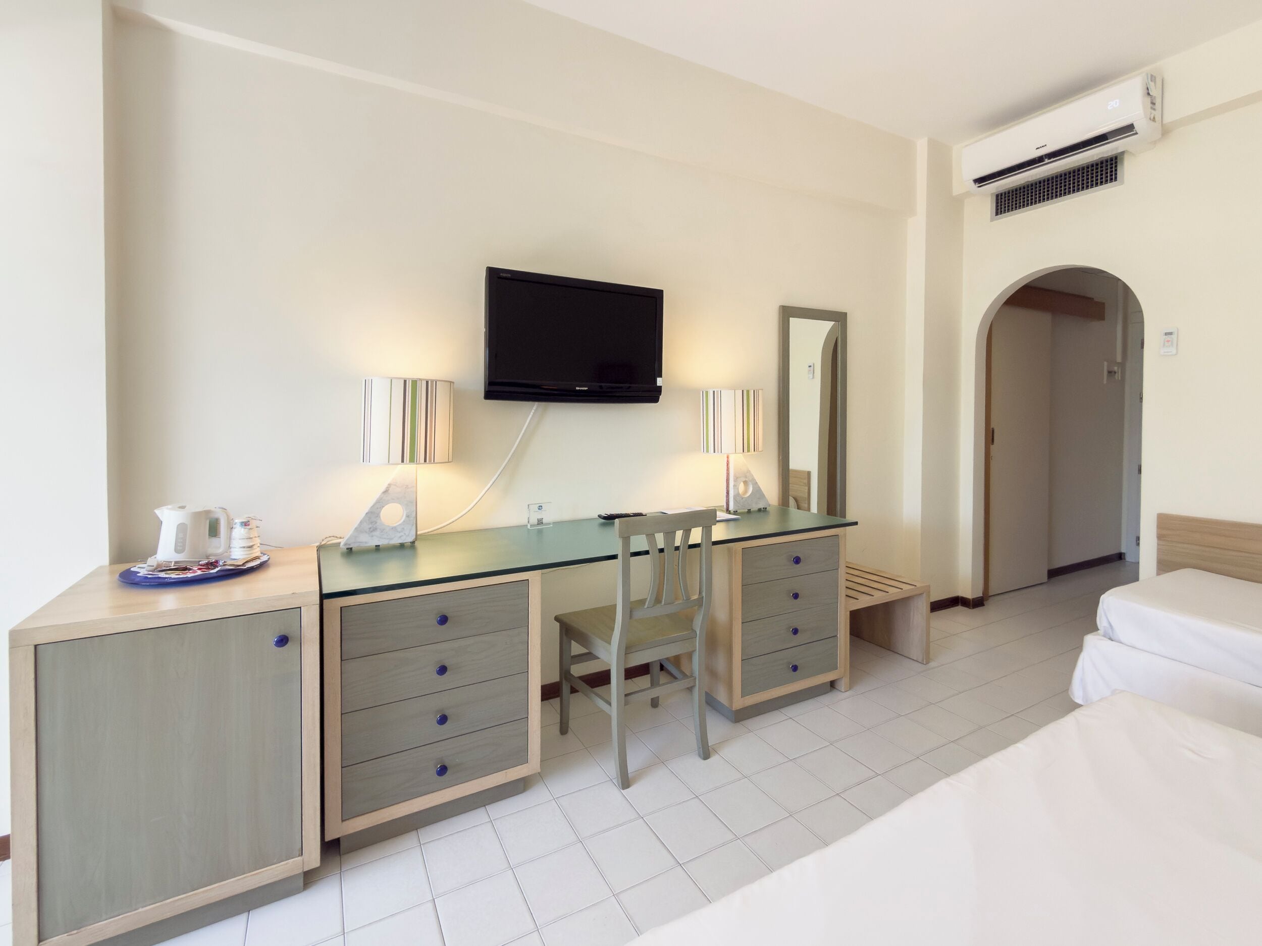 Habitación de hotel con cama, escritorio con cajones, silla, televisor montado en la pared y equipo de aire acondicionado.