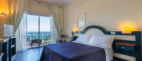 A hotel room with a bed, bedside table, lamp, and a TV. There is a balcony with a chair and a table.