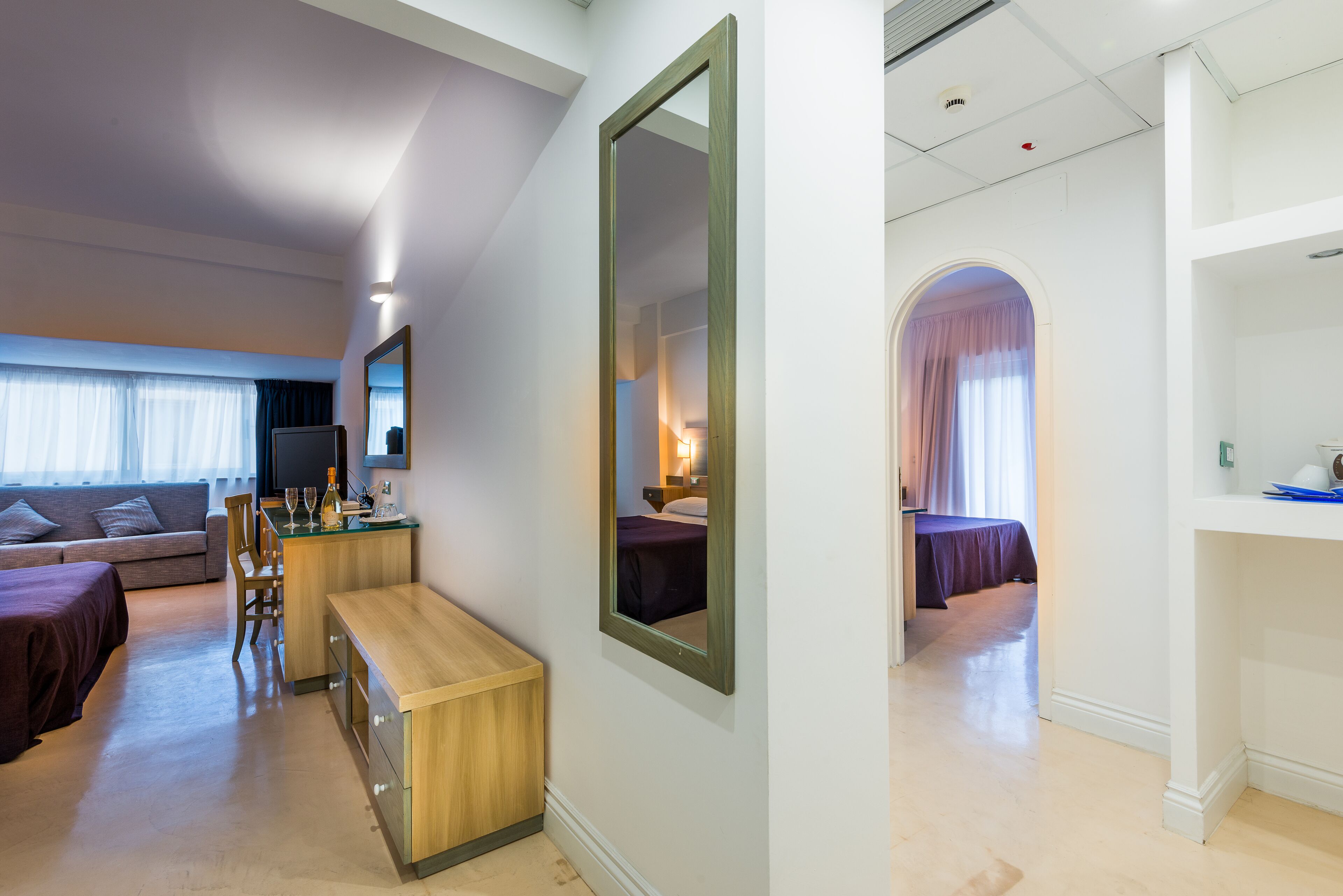 Moderni hotellihuone, jossa on sohva, puinen työpöytä, peili ja sänky.