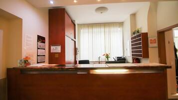 A reception desk with a wooden finish, a bulletin board with notices, and a window with blinds in the background.