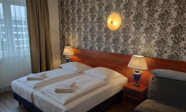 Une chambre d’hôtel avec deux lits, une tête de lit en bois, un papier peint à motifs et deux lampes de chevet.