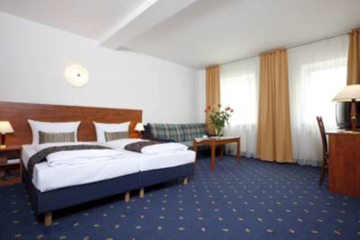 A hotel room with a bed, a nightstand, a desk, a chair, and a window with curtains.