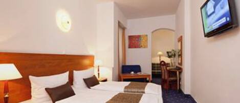 A hotel room with a large bed, a desk, a chair, a television, and a small table with a lamp.