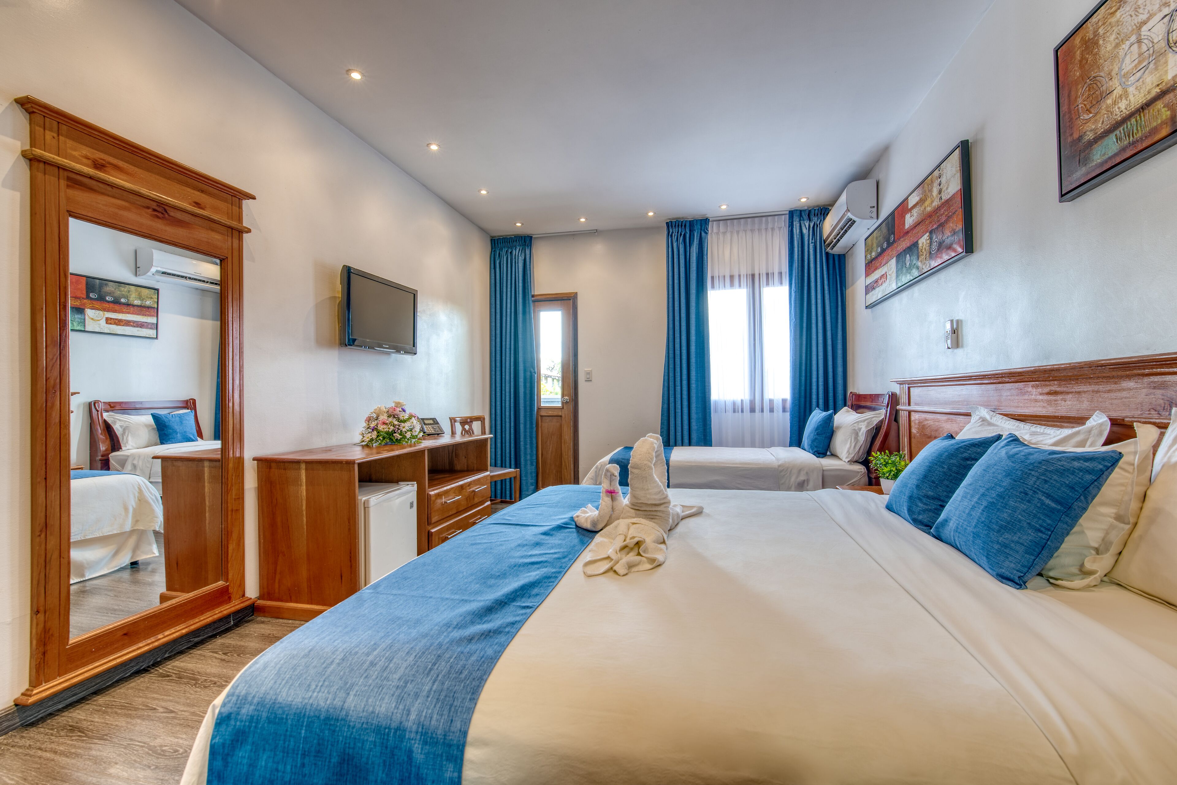Quarto de hotel com uma cama grande, uma mesa, uma cadeira, uma TV e um espelho.
