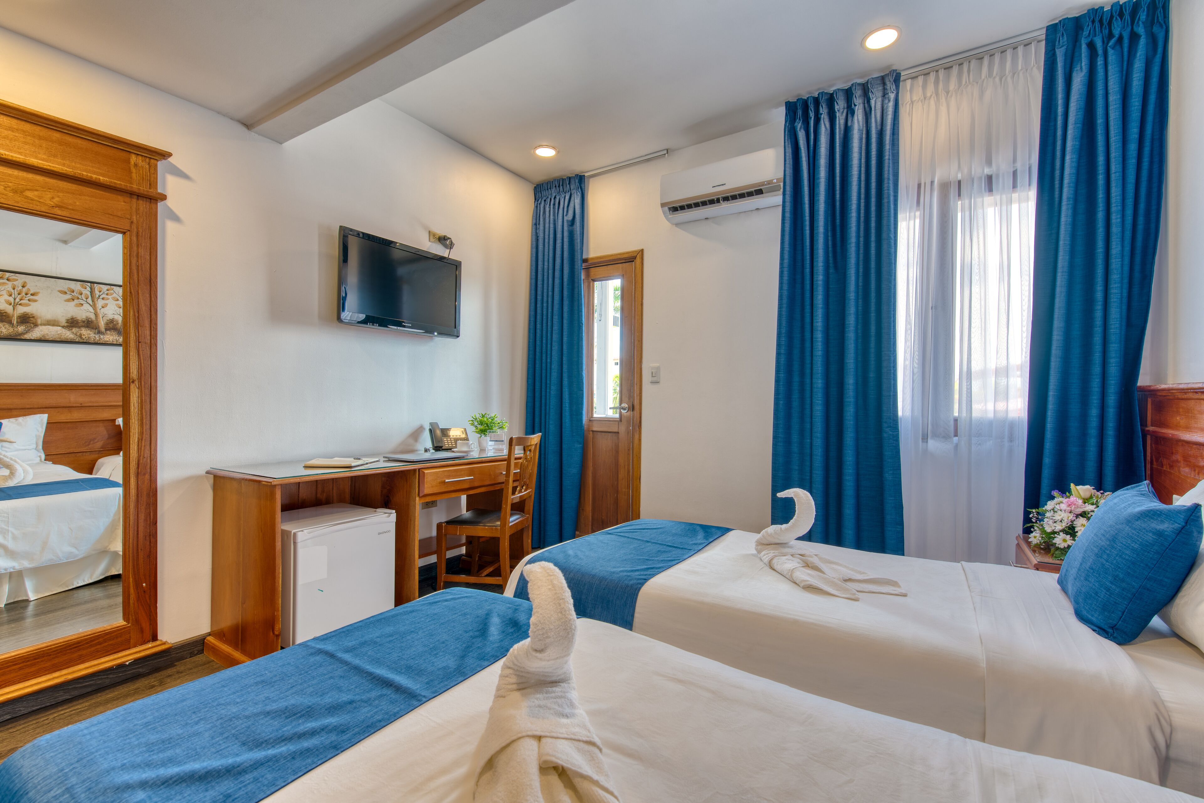 Quarto de hotel com duas camas, uma escrivaninha, uma cadeira, uma televisão e um ar condicionado.