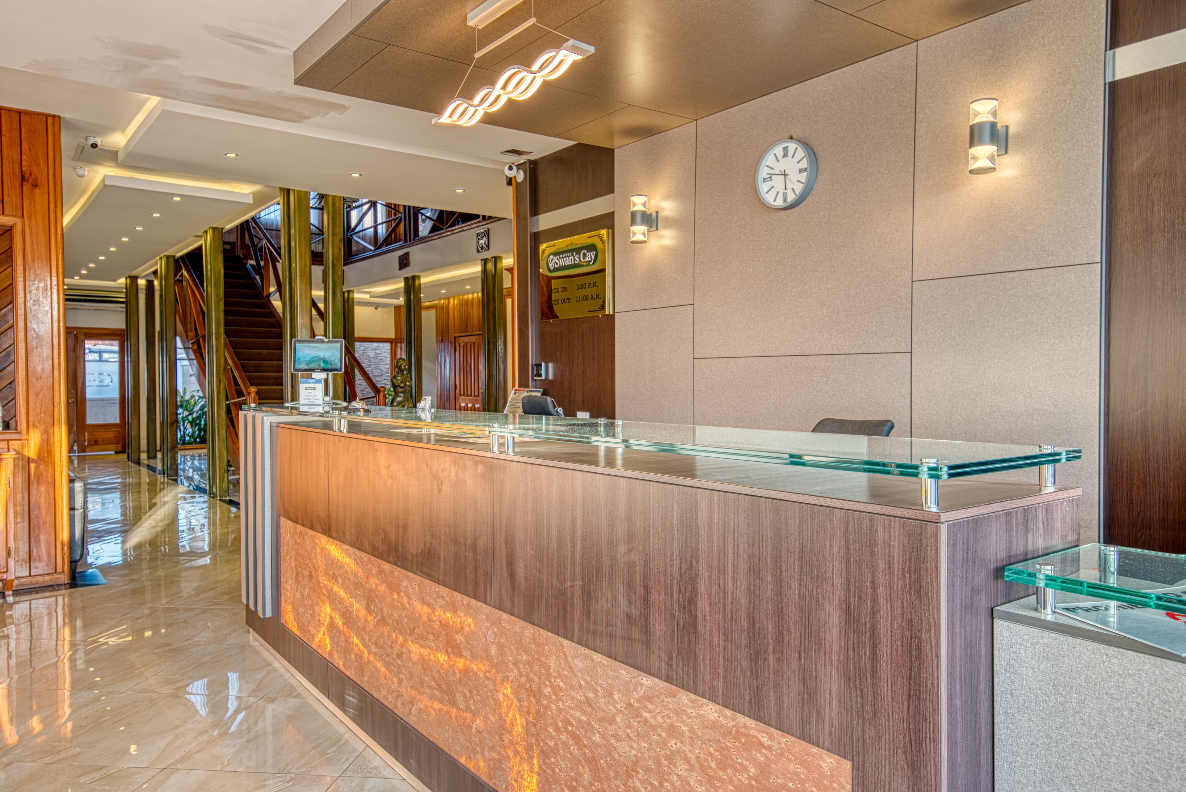 A modern reception area with a glass counter, wooden accents, a clock, and a staircase leading to upper levels.