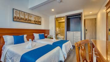 Ein Hotelzimmer mit zwei Betten, einem hölzernen Kopfteil, einem Bild an der Wand, einem sichtbaren Badezimmer durch eine offene Tür und einem Holztisch.