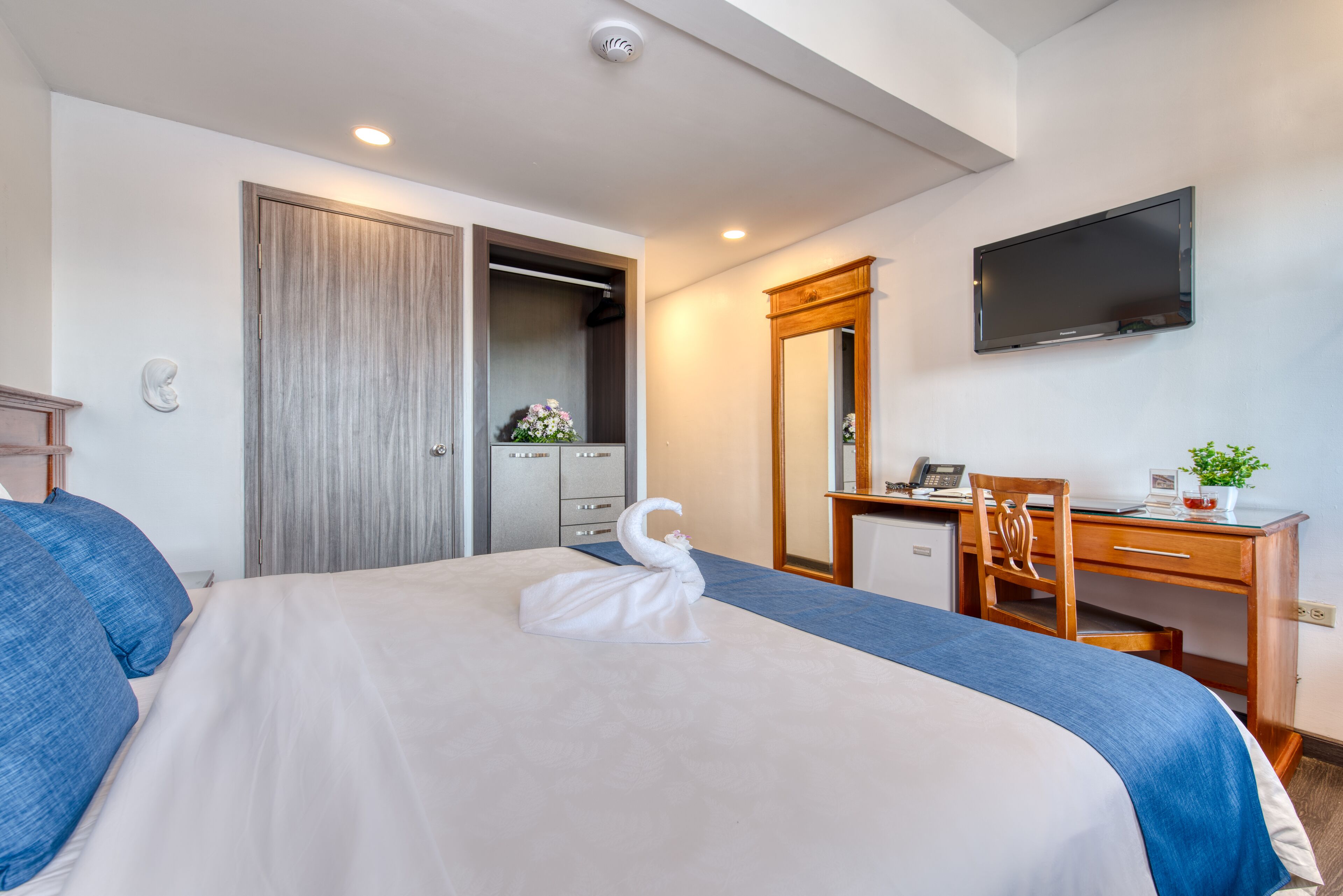 Una habitación de hotel con una cama grande, un escritorio con silla, un televisor en la pared y un armario.