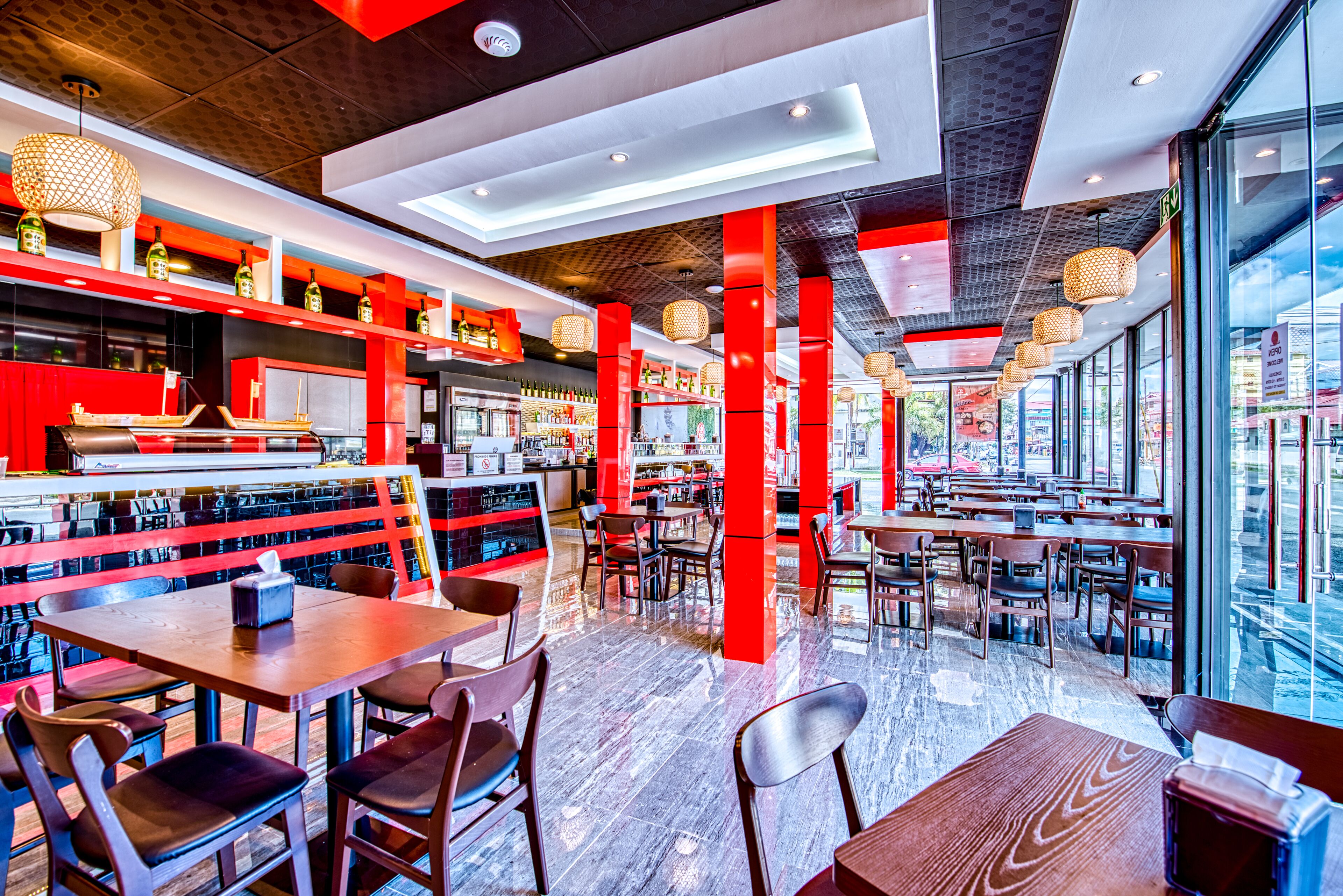Een modern restaurantinterieur met rode accenten, houten tafels en een bar.