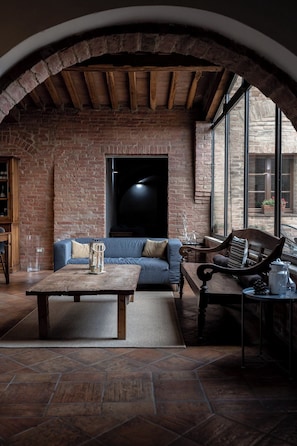 A cozy room with a brick wall, a wooden ceiling, a sofa, a coffee table, and a window with a view. - Hotel More di Cuna (Monteroni d'Arbia)