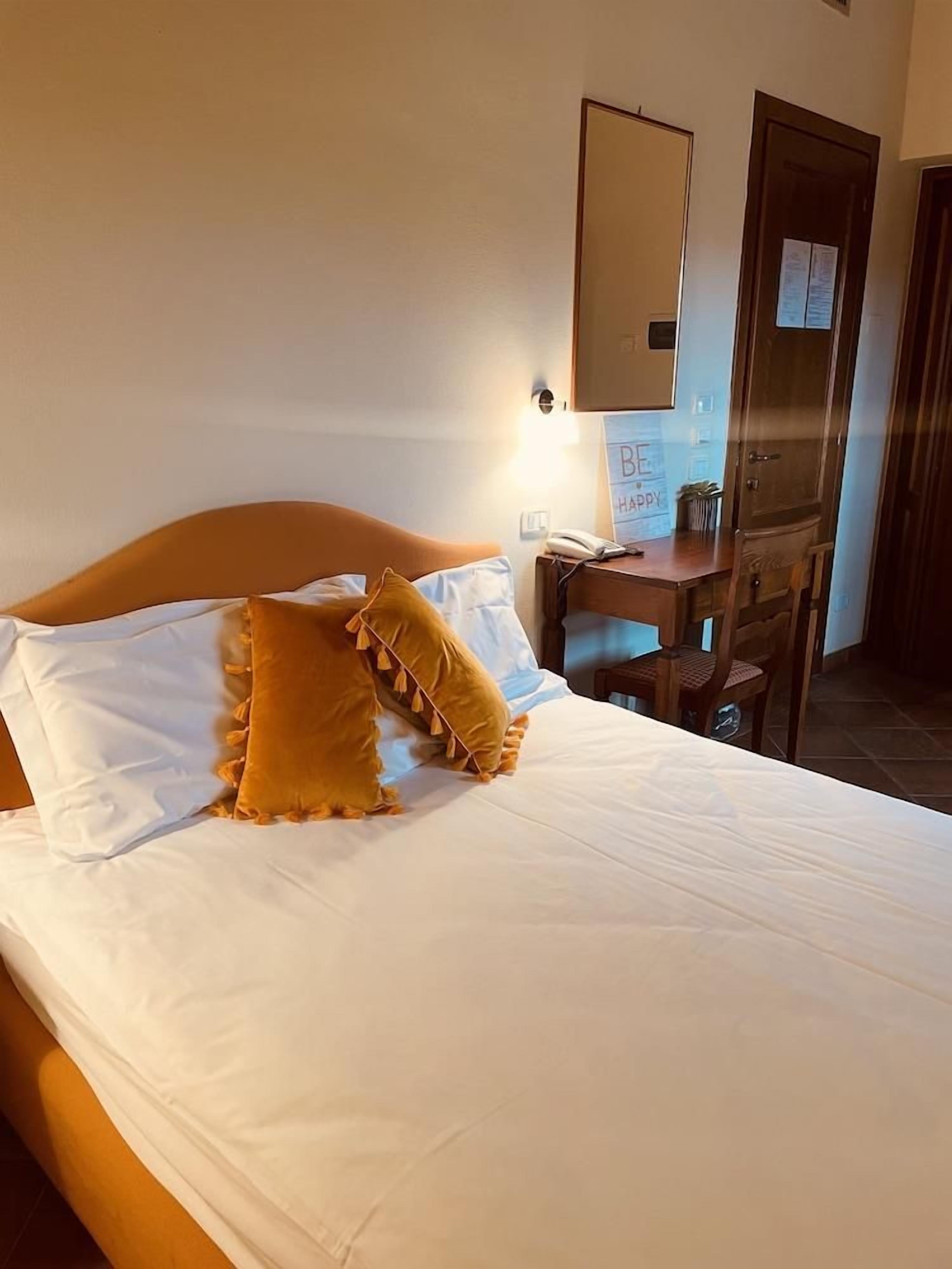 A hotel room with a bed, a desk, a chair, and a mirror on the wall.
