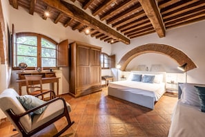 Une chambre à coucher avec un grand lit, des meubles en bois, un bureau et une fenêtre donnant sur les arbres.
