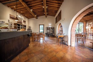 A spacious dining area with wooden tables and chairs, a counter with food items, and a brick wall with a window.
