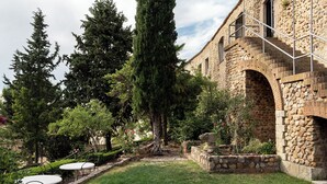 A courtyard with a stone building, a grassy area, and a tall tree. - Parador de Ciudad Rodrigo (Ciudad Rodrigo)