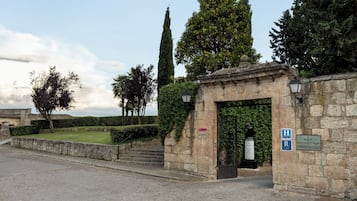 A stone building with a gate, a sign indicating a hotel, and a paved street.
