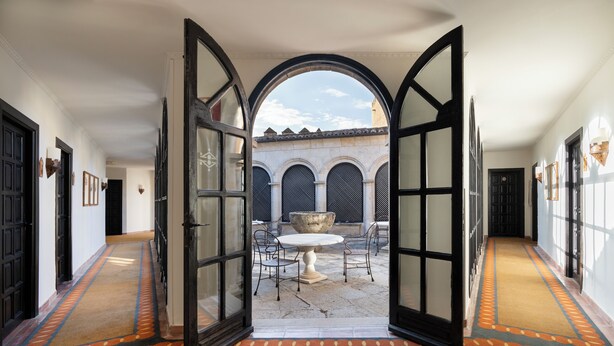 An open archway leading to a courtyard with a table and chairs, surrounded by walls with arched windows and a tiled floor. - Parador de Ciudad Rodrigo (Ciudad Rodrigo)