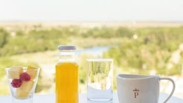 A breakfast setting with pastries, a glass of juice, and a cup with a spoon on a table with a scenic view in the background.