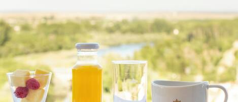 A breakfast setting with pastries, a glass of juice, and a cup with a spoon on a table with a scenic view in the background.