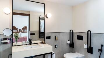 Un bagno moderno con uno specchio grande, un lavabo e un water. Sono presenti luci a parete e un porta asciugamani.