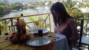 A dining table set outdoors with a view of a river and mountains. - Le Bamboo (Mahebourg)