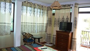A room with a bed, a television on a wooden cabinet, a dining table with chairs, and patterned curtains. - Le Bamboo (Mahebourg)