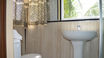 Une salle de bain avec des toilettes, un lavabo et une fenêtre donnant sur des palmiers.