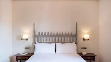 Una cama bien tendida con sábanas blancas, dos mesitas de noche con lámparas, y un aplique en la pared.