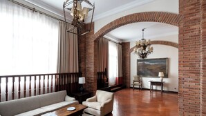 A spacious living room with a brick wall, a large window with curtains, a sofa, a coffee table, and a chandelier. - Parador de Calahorra (Calahorra)