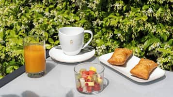 Una mesa con un vaso de jugo de naranja, una taza con un logotipo, un plato de pasteles y un bol de fruta.