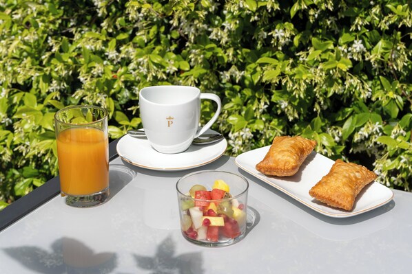 Una mesa con un vaso de jugo de naranja, una taza con un logotipo, un plato de pasteles y un bol de fruta.
