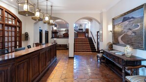 A spacious lobby with a wooden reception desk, hexagonal tiled flooring, and a staircase leading to upper floors. - Parador de Calahorra (Calahorra)