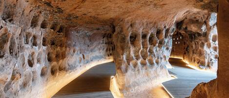 Un interior con formaciones rocosas naturales, suelo de madera y un pasaje central en arco.