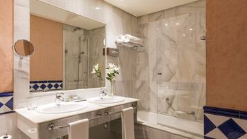 Een moderne badkamer met twee wasbakken, een grote spiegel, een douche met glazen wand en een toiletrolhouder.