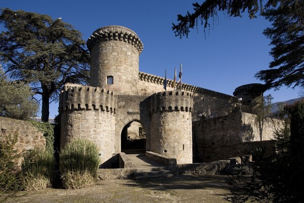 Un castillo de piedra histórico con una torre redonda, una entrada en arco y banderas.