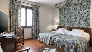 Habitación de hotel con dos camas, un escritorio, una silla y una mesa con un libro y gafas.