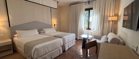Habitación de hotel con dos camas, una mesita redonda pequeña, un sofá y un televisor.