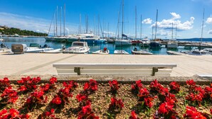 Un port de plaisance avec des bateaux amarrés, un banc blanc et des fleurs rouges au premier plan.