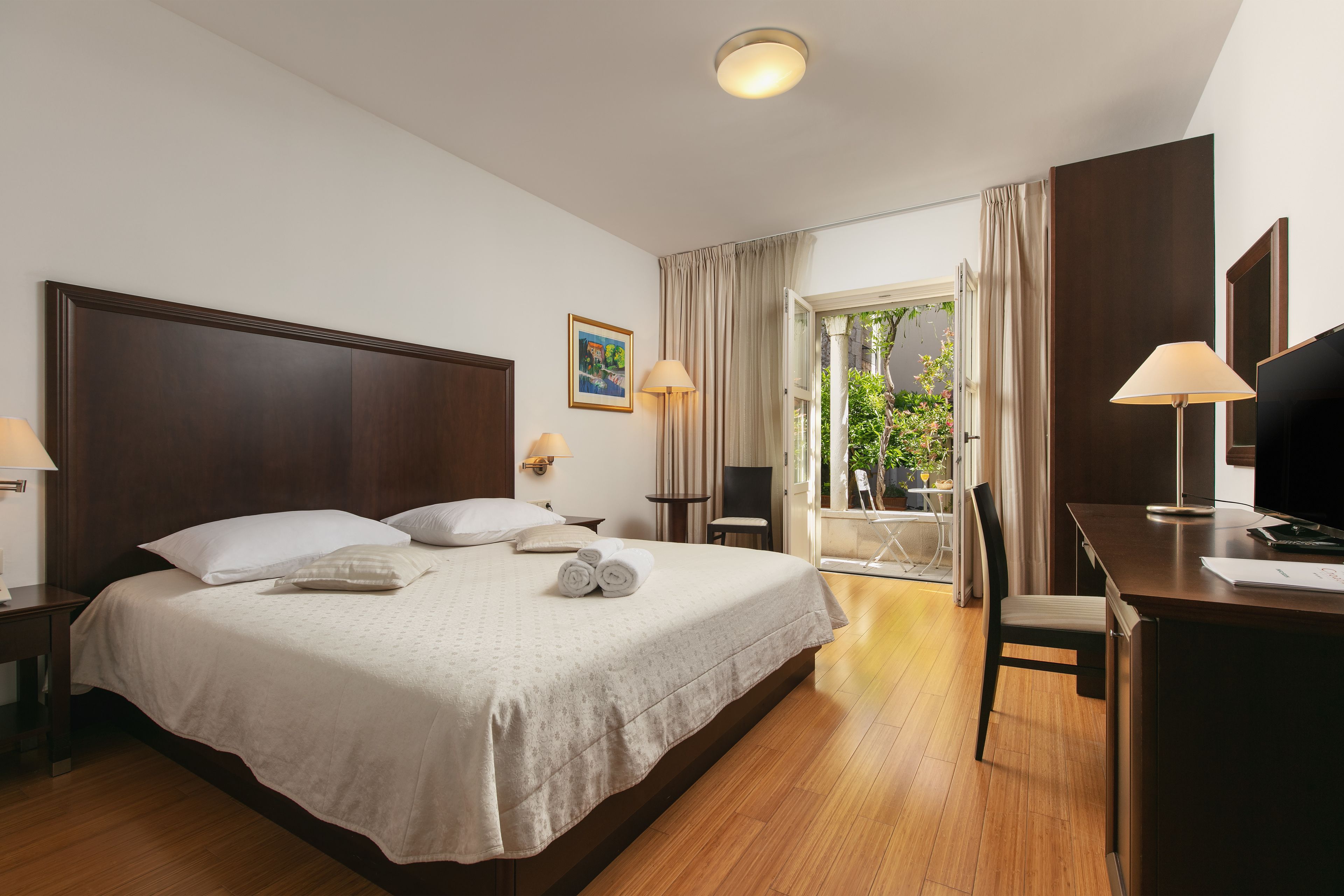 A hotel room with a large bed, a desk, a chair, and a balcony with curtains.