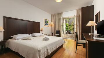 A hotel room with a large bed, a desk, a chair, and a balcony with curtains.