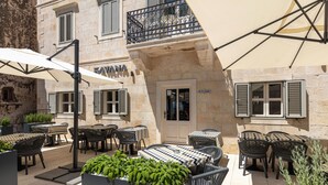 Une terrasse extérieure avec des tables et des chaises, un parasol blanc et des plantes en pot.
