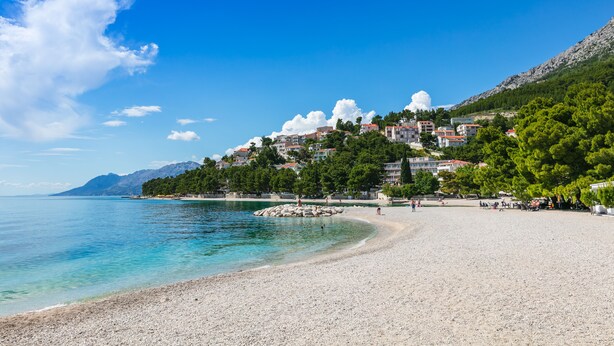 Une ville côtière avec une plage de galets, des bâtiments construits sur une colline et un ciel bleu dégagé.