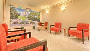 A hotel lobby with red upholstered chairs, a wooden table, and a mural of a building on the wall. - 121 Paris Hotel (Paris)