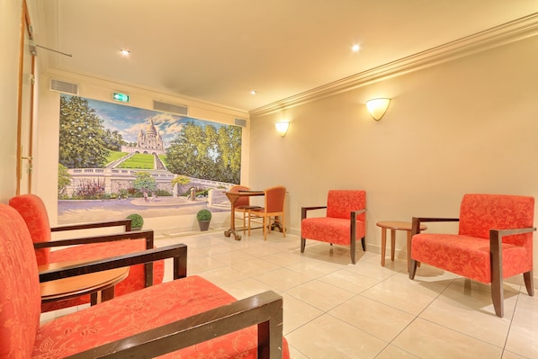 Un hall de hotel con sillones tapizados en rojo, una mesa de madera y un mural de un edificio en la pared.