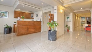 A hotel lobby with a reception desk, wooden cabinets, potted plants, and a tiled floor. - 121 Paris Hotel (Paris)