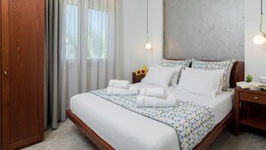 Un letto rifatto con cura, con una coperta a motivi geometrici, una testiera in legno e un comodino con una lampada.