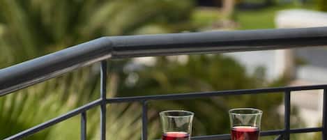 Balcón con dos copas de vino y un libro, con vistas a la costa, zonas verdes y un puente distante.